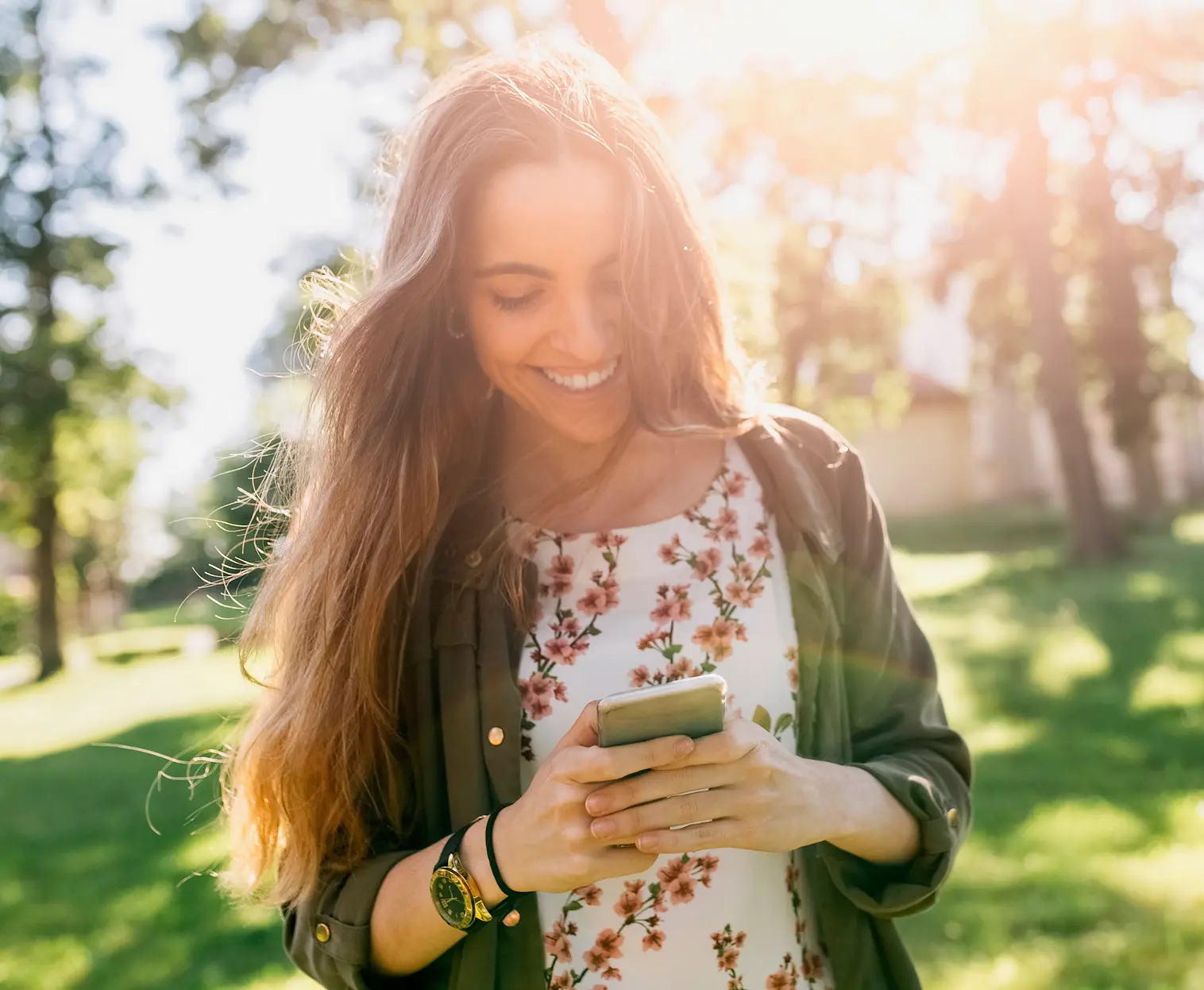 Junge Frau in Park blickt lächelnd auf Ihr Smartphone.